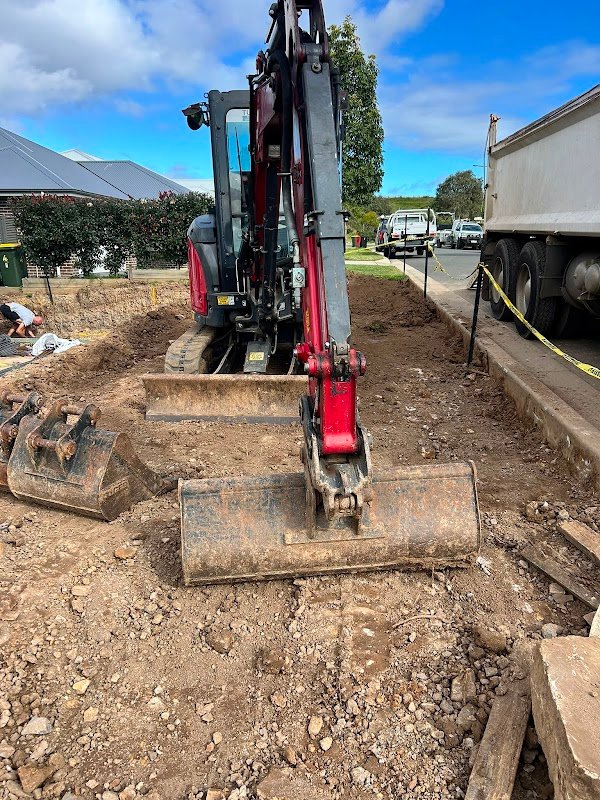 Red mini excavator at residential site with tip truck waiting