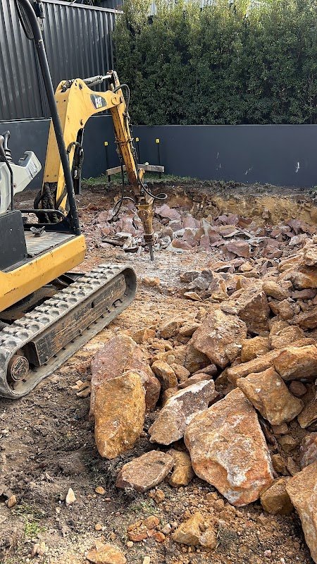 Compact excavator breaking sandstone with hydraulic hammer