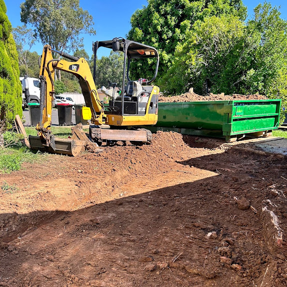 Excavator loading spoil into a skip bin during a service trench dig